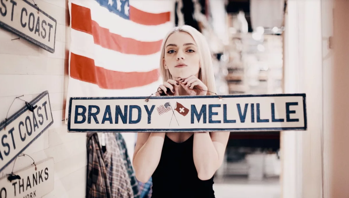 blonde girl holding a Brandy Melville sign in a Brandy Melville boutique